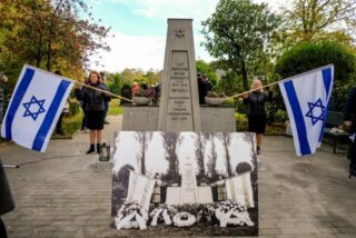 Ein Mahnmal, flankiert von zwei Frauen mit israelischen Flaggen in den Händen.