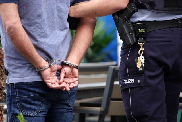 Ein Polizist führt einen Mann in Handschellen ab. (Symbolbild)