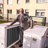 Ein Mann steht an zwei Luft-Wasser-Wärmepumpen vor einem Mehrfamilienhaus in Recklinghausen.