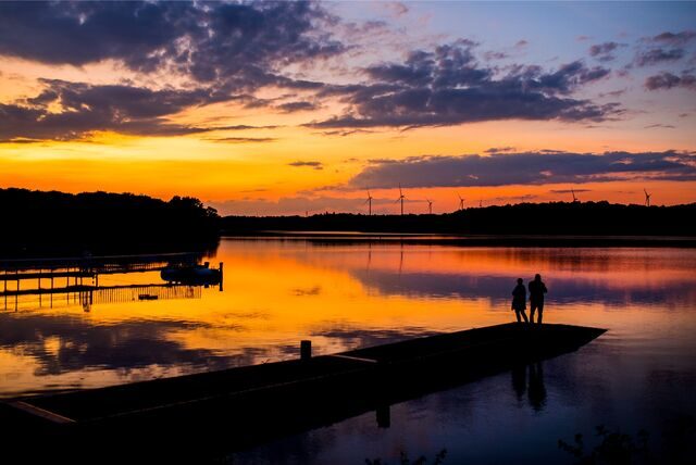 Zwei Personen stehen in Haltern am See bei untergehender Sonne auf einem Steg am Halterner Stausee.