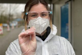 Eine Frau in Schutzkleidung nimmt einen Corona-Abstrich vor
