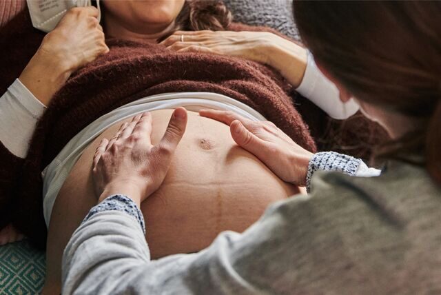 Eine Hebamme tastet in ihrer Praxis den Bauch einer schwangeren Frau ab.