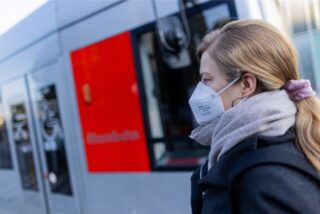 Eine Frau mit FFP2-Maske wartet auf ihre Straßenbahn