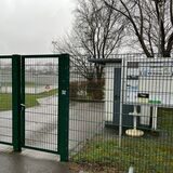 Ein Zaun rund um das Hirschkamp-Stadion in Waltrop, dahinter ist ein Schaukasten zu sehen und der Sportplatz.
