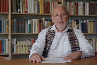 Wolfgang Gerlach sitzt vor einem Bücherregal