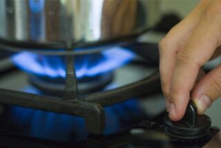 Eine Frau regelt an einem Herd die Gasflamme.