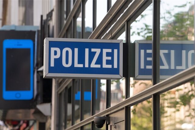 Ein Schild mit der Aufschrift „Polizei“ hängt am 1. Polizeirevier vor dem Schild eines Handygeschäfts, das die Form eines Smartphones hat.