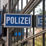 Ein Schild mit der Aufschrift „Polizei“ hängt am 1. Polizeirevier vor dem Schild eines Handygeschäfts, das die Form eines Smartphones hat. 