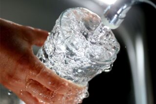Klares Wasser fließt aus einem Wasserhahn in einer Glas.