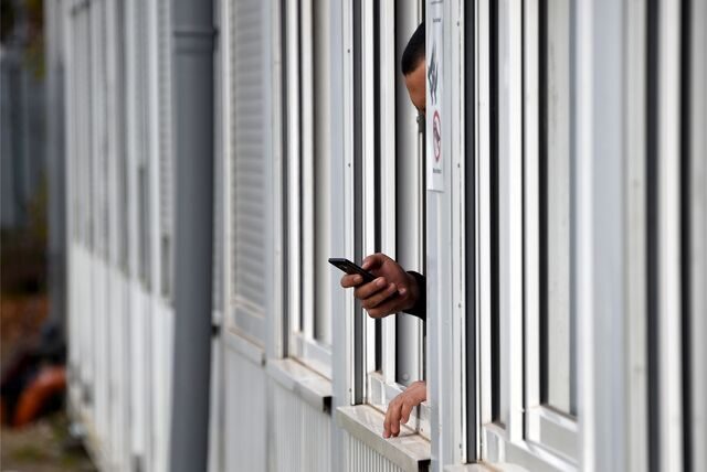 Ein Mann hält in einem Wohncontainer sein Smartphone aus dem Fenster.