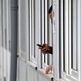 Ein Mann hält in einem Wohncontainer sein Smartphone aus dem Fenster.