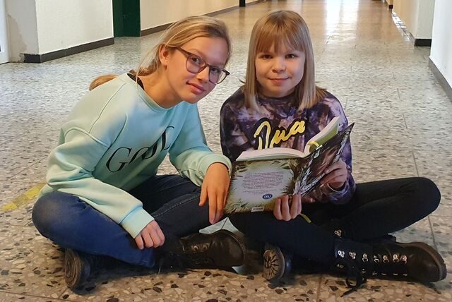 Zwei Mädchen sitzen auf dem Boden und lesen ein Buch.