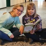 Zwei Mädchen sitzen auf dem Boden und lesen ein Buch.