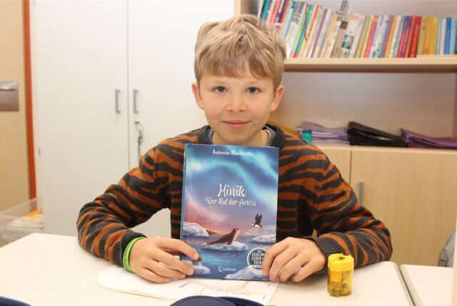 Justus (10), Schüler der August-Hermann-Francke-Schule Waltrop, sitzt an seinem Tisch und hält das Buch „Minik – Der Ruf der Arktis“ in die Kamera.