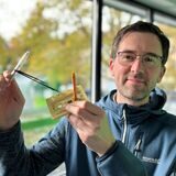 Papatastisch-Autor Thomas Raulf hält eine Hörspielkassette mit zwei Stiften