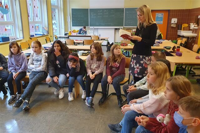 Autorin Britt Glaser steht zwischen Kindern in einer Schulklassen und liest aus einem Buch