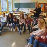 Autorin Britt Glaser steht zwischen Kindern in einer Schulklassen und liest aus einem Buch