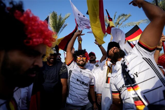Fußball-Fans in Deutschland-Trikots schwenken Deutschland-Fahnen unter Palmen in Katar