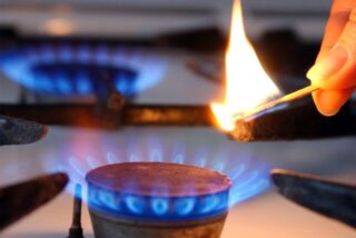Mit einem Streichholz wird die Flamme eines Gasherdes entzündet.