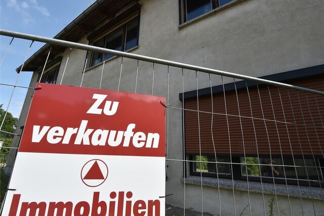 An einem Bauzaun vor einem Haus hängt ein Schild mit der Aufschrift „zu verkaufen“.