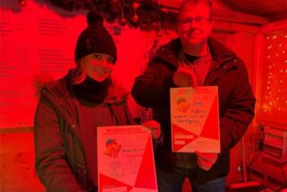 Zwei ehrenamtliche Helfer stehen mit Wunschzetteln in der „Hütte der guten Taten“ auf dem Weihnachtsmarkt Recklinghausen