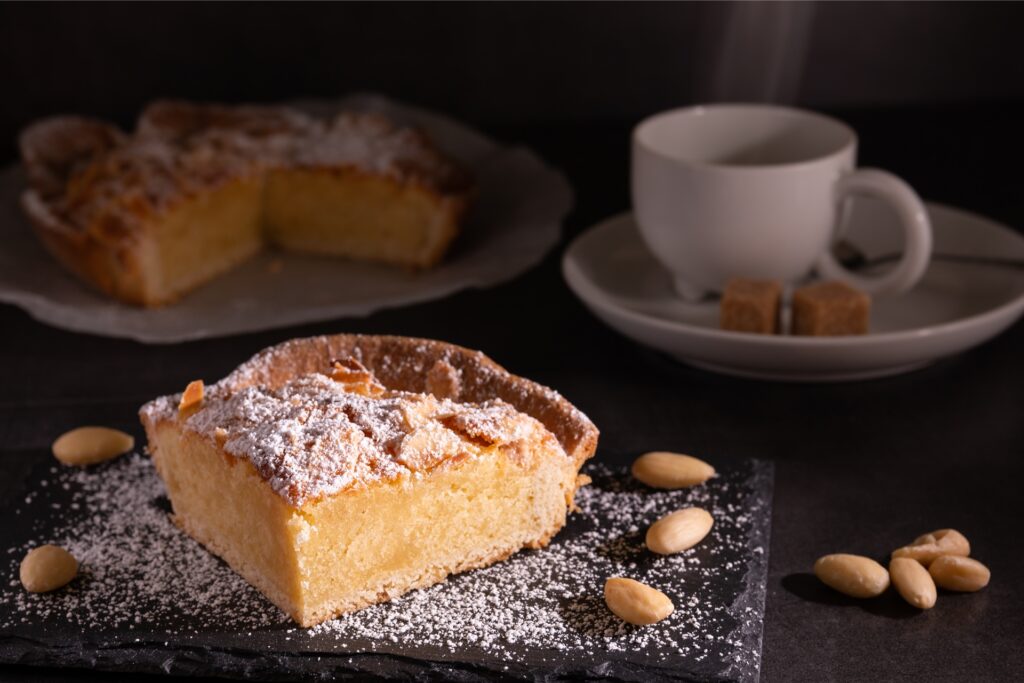 ein stück kuchen, mandeln und ein ganzer kuchen mit kaffee im hintergrund