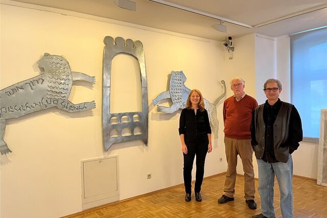 Abi Shek, Kathrin Pieren und Thomas Redder stehen vor einem Kunstwerk, das einen Toraschrein und zwei Löwen zeigt.