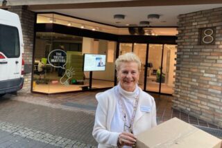 Eine Frau steht mit einem Paket in der Hand vor einem Ladenlokal.