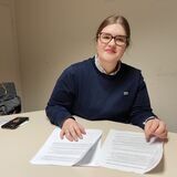 Eine junge Frau mit Brille sitzt an einem Tisch.