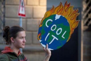 Eine „Fridays for Future“-Aktivistin hält ein Plakat mit einer brennenden Erde und der Aufschrift „Cool it“.