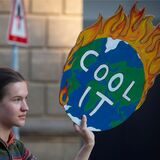 Eine „Fridays for Future“-Aktivistin hält ein Plakat mit einer brennenden Erde und der Aufschrift „Cool it“.