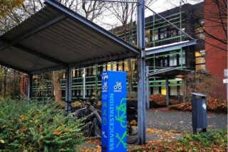 Ein blauer Metallschrank mit dem Aufdruck Servicestation steht vor einem Verwaltungsgebäude.