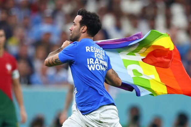 Ein Flitzer mit der Regenbogenflagge und politischen Botschaften zur Ukraine und Iran auf dem T-Shirt läuft über den Rasen.