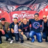 Mehrere Musiker hocken für ein Bandfoto Arm in Arm nebeneinander. Im Hintergrund ist der Schriftzug „The Servants“ zu sehen.