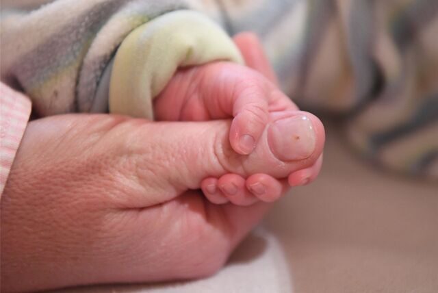 Eine Babyhand hält einen Finger eines Erwachsenen.