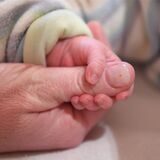 Eine Babyhand hält einen Finger eines Erwachsenen.