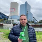 Ein Mann steht mit einem Mikrofon in der Hand am Ufer des Kanals in Datteln, im Hintergrund ein Kraftwerk.