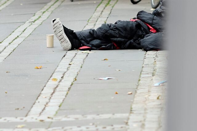 Ein Mann sitzt in einen Schlafsack gehüllt auf dem Asphalt.