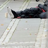 Ein Mann sitzt in einen Schlafsack gehüllt auf dem Asphalt.