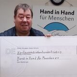 Detlef „Didi“ Pourie (links) steht mit einem Scheck über 4770 Euro neben Rüdiger Engler vom Verein „Hand in Hand für Menschen“.
