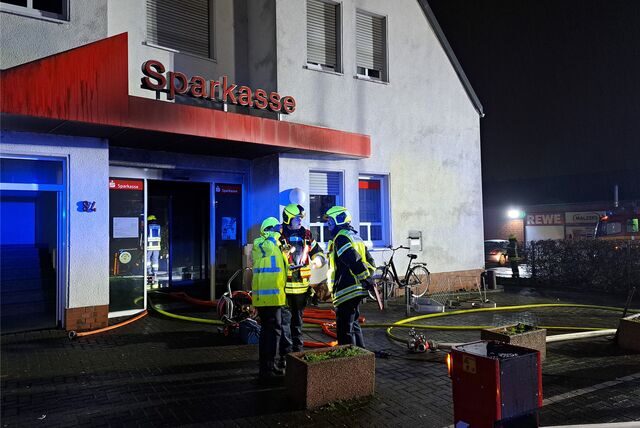 Feuerwehrkräfte stehen vor der Sparkassenfiliale am Bachackerweg, nachdem sie den Brand gelöscht haben.