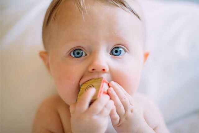 Ein Baby mit blauen Augen spielt mit einem Holzwürfel.