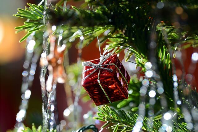 Ein kleines rotes Geschenkpaket als Weihnachtsbaumanhänger und Lametta hängen an einem Weihnachtsbaum.