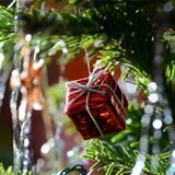 Ein kleines rotes Geschenkpaket als Weihnachtsbaumanhänger und Lametta hängen an einem Weihnachtsbaum.