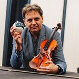 Misha Nodelman hält in seiner linken Hand eine Christbaumkugel, in der rechten Hand seine Geige.