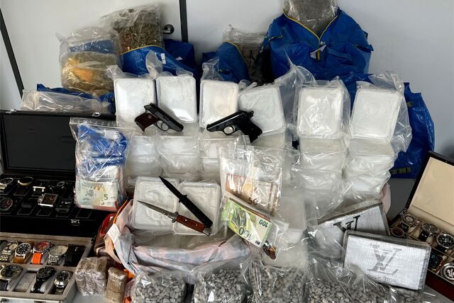 Auf einem Tisch stehen mehrere Pakete verschiedener Drogen, Messer, Bargeld, Pistolen und Uhren.