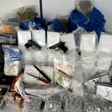 Auf einem Tisch stehen mehrere Pakete verschiedener Drogen, Messer, Bargeld, Pistolen und Uhren.