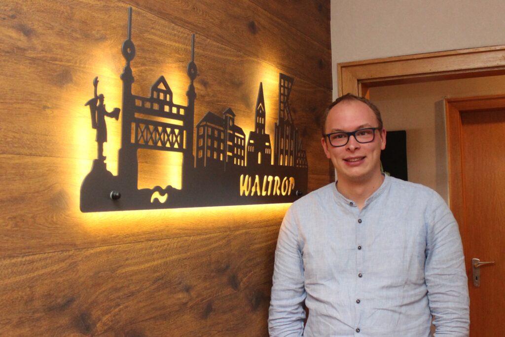 Der Waltroper Frédéric Baumhöfner in seiner Wohnung in Waltrop vor einer beleuchteten Waltrop-Stadtsilhoutte.