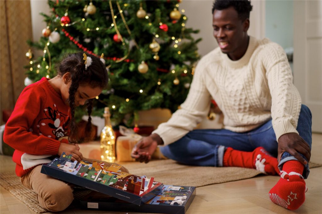 papa schaut seiner tochter beim auspacken eines adventskalenders zu