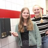 Rebecca Winterberg (re.) und Charlotta Coumans von der Schülervertretung am Theodor-Heuss-Gymnasium in Waltrop stehen neben einem Periodenprodukte-Spender in einer der Schultoiletten.